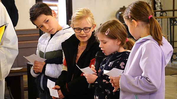 Vier Kommunionkinder stehen nebeneinander, um Fürbitten vorzulesen