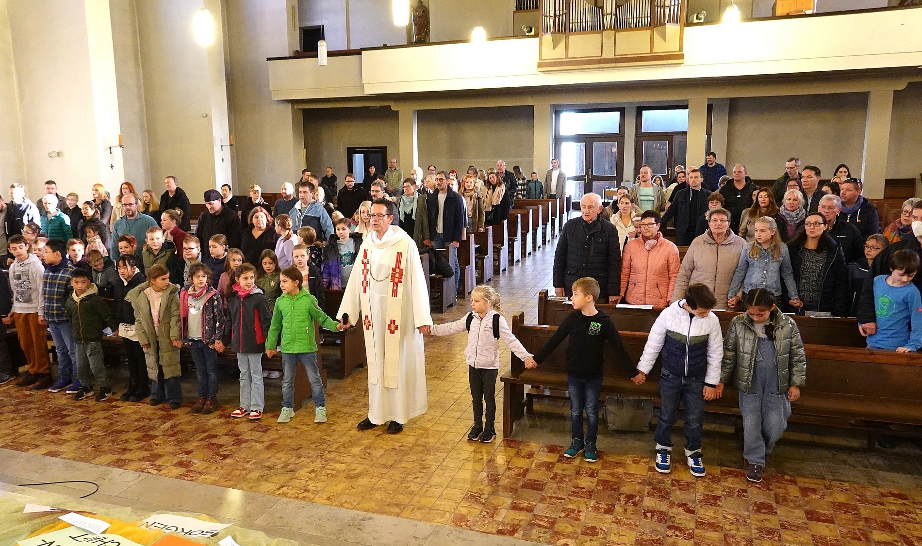 Der Pfarrer steht im Mittelgang und reicht den Kommunionkindern in der ersten Reihe die Hände